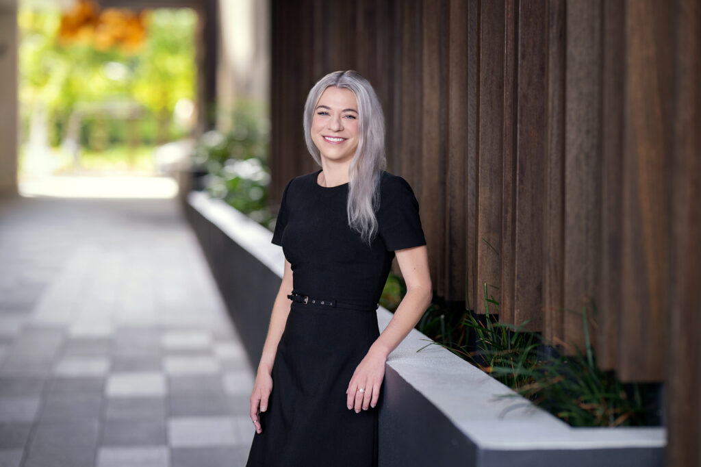 Jeri Murray - Hall Payne Lawyers - smiling and leaning against wall planter