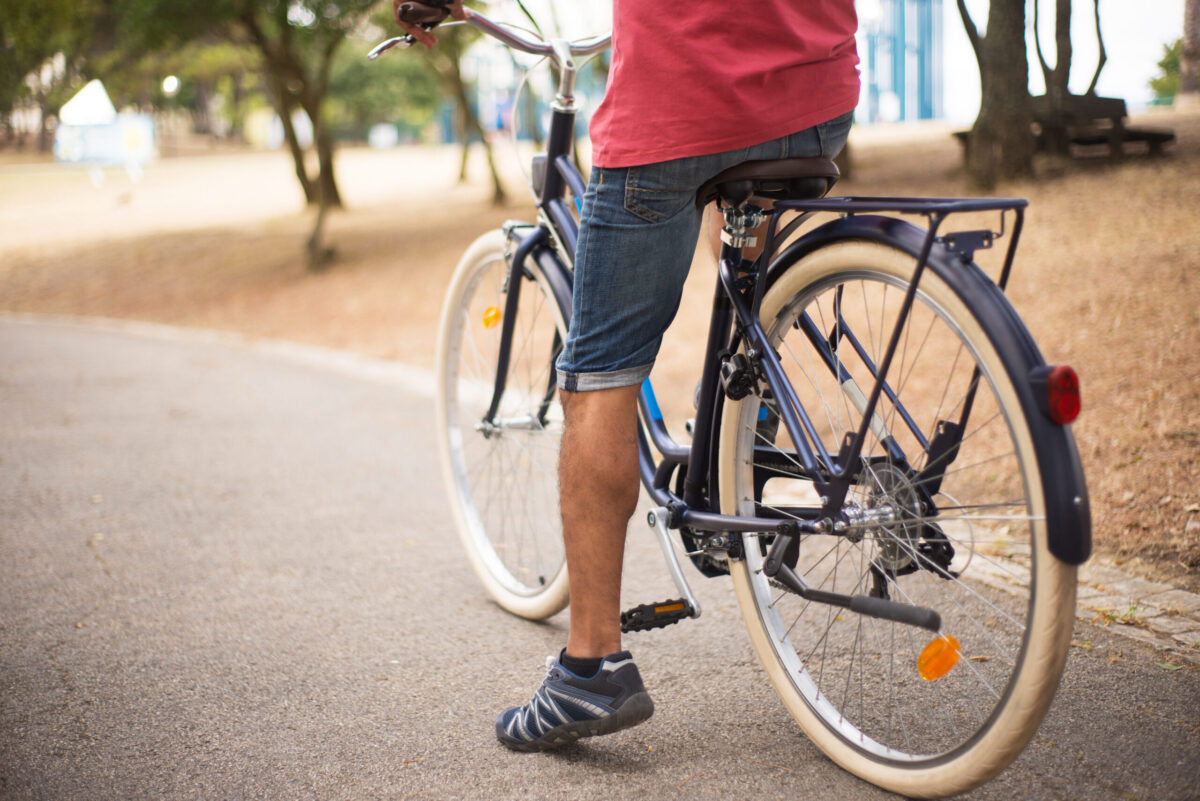 Close-up of man riding bicycle along sidewalk.